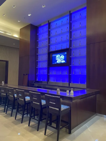 Backlit blue bar in the Owners Club with bottle shelves and the Cowboys game on a screen