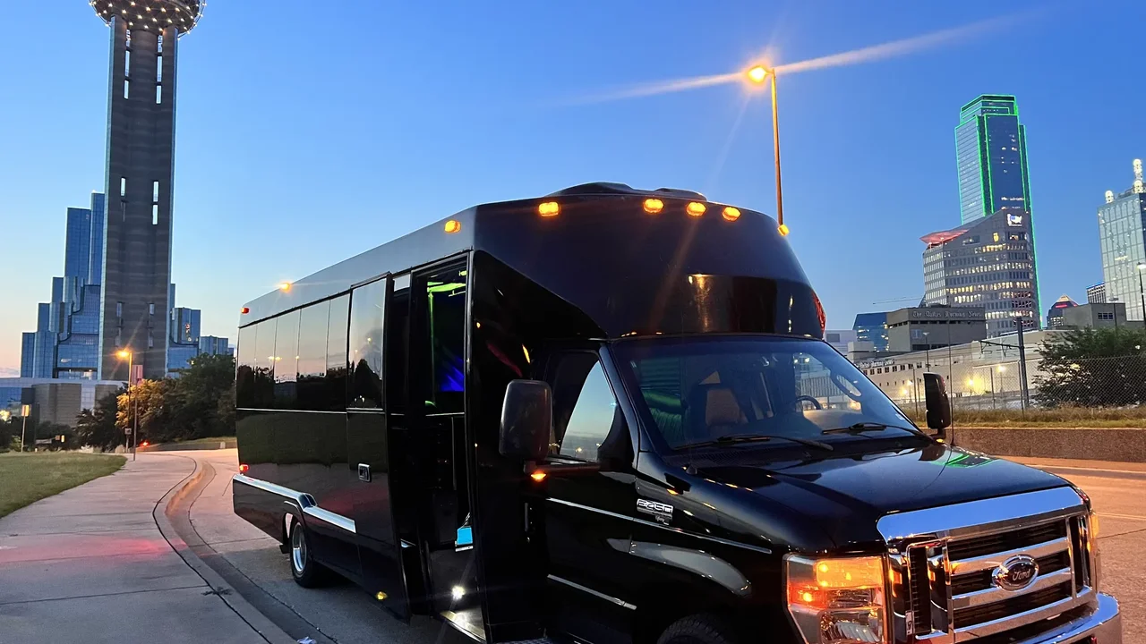 A black party bus parked under Reunion Tower and the Dallas skyline at dusk